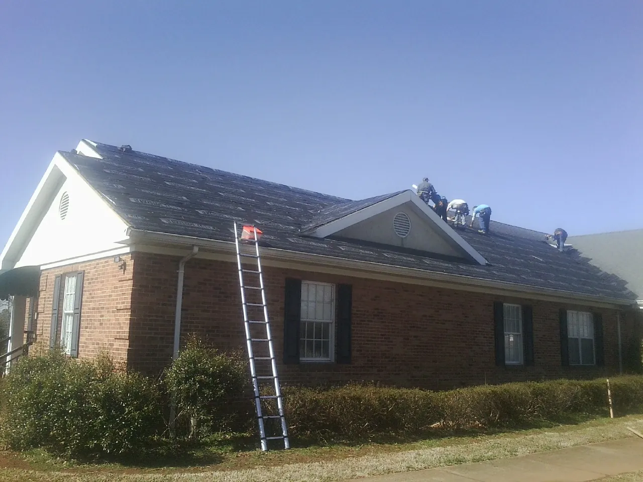 Crew tearing shingles off a brick ranch roof with a ladder set — Emergency Roof Repair work by our crew in Lockbourne