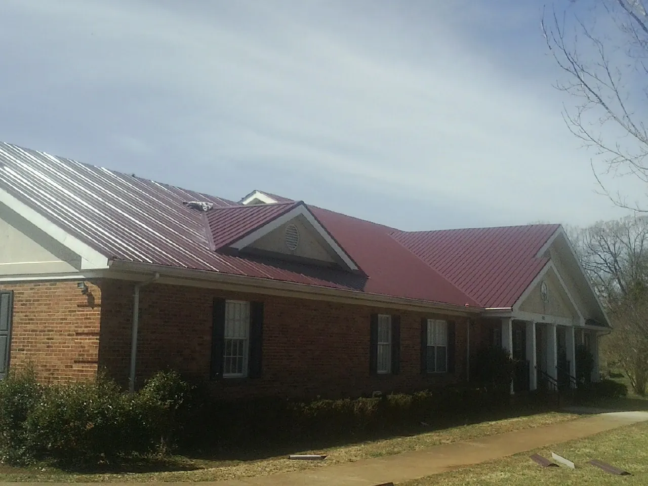Red metal roof with gabled entries on a long brick building, from a Hail Damage Roof Repair job in Lockbourne