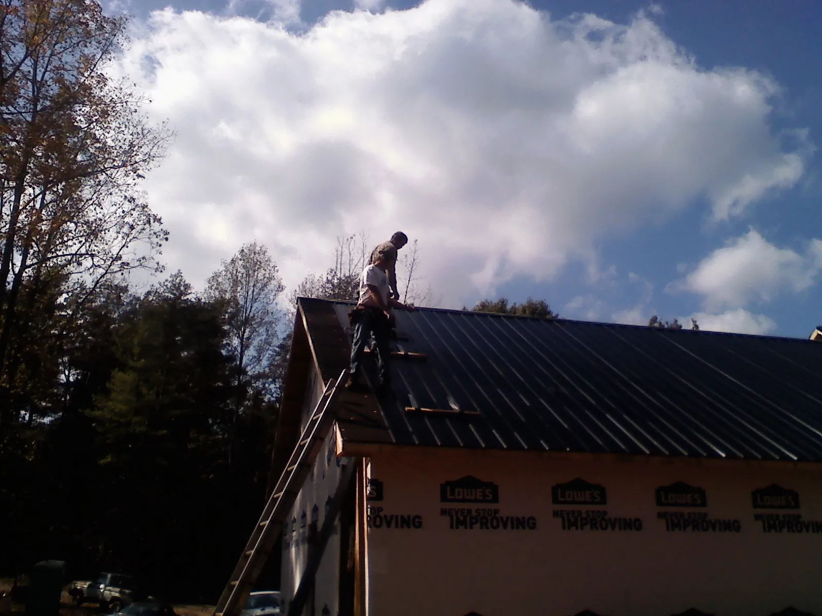 Roofer fastening dark metal panels high against a cloudy sky, from a Roof Inspection job in Lockbourne
